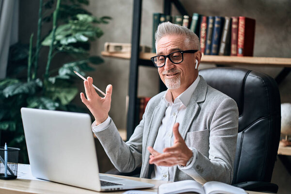 Happy gray-haired businessman in gray jacket talking during video conference at his workplace. Business concept