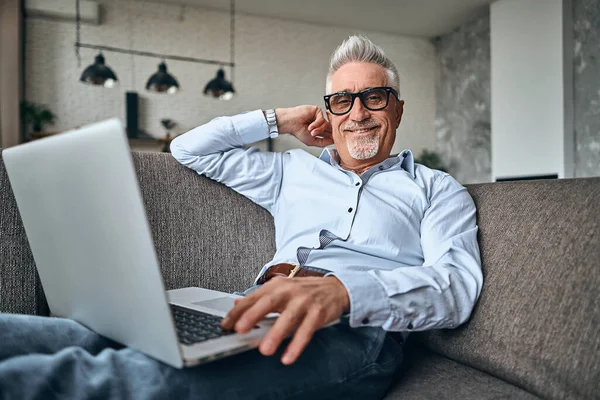 Hombre Adulto Sonriente Descansando Casa Mientras Trabaja Con Ordenador Portátil — Foto de Stock