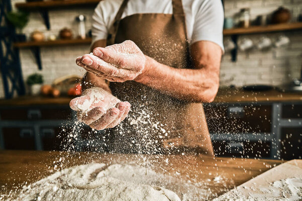 Close up of male hands sprinkling dough with flour while cooking on the kitchen. Baking process concept