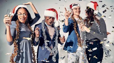 Gri arka planda izole edilmiş havalı bir parti yaparken ellerinde şampanya bardaklarıyla mutlu genç erkekler ve kadınlar. Noel konsepti