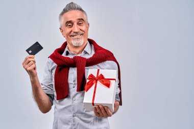 Siyah kredi kartı ve hediye kutusuyla stüdyoda duran gülümseyen olgun bir adam. Boşluğu kopyala