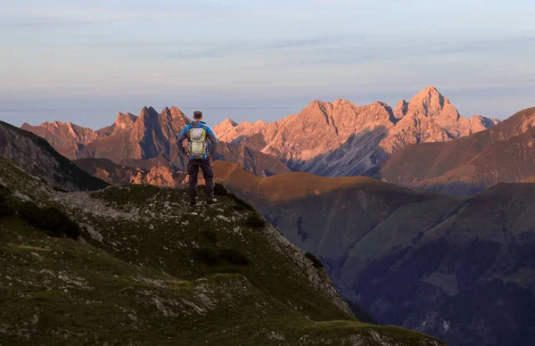 Hombre excursionista de pie ante una vista increíble desde la alta montaña hasta muchos otros picos en Sunset. Allgau, Baviera, Alpes, Alemania. — Foto de Stock