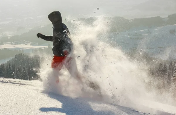 Homem feliz com capuz correndo em neve de pó profundo com sapatos de neve. Neve está pulverizando e salpicando. — Fotografia de Stock