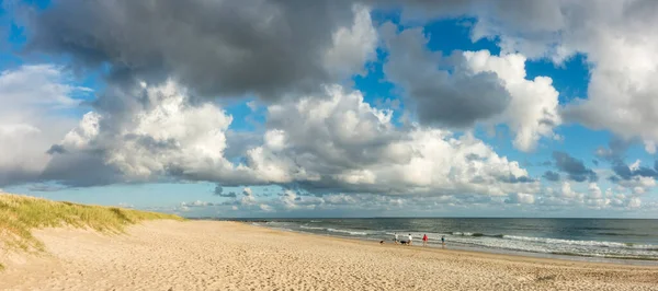 Spiaggia sabbiosa panoramica con persone e cani. Cielo azzurro e nuvole drammatiche sul lungomare in morbida luce del tramonto serale. Hvidbjerg Strand, Blavand, Mare del Nord, Danimarca. — Foto Stock