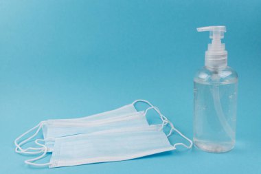 Yüz maskeleri ve el dezenfektanı mavi arka planda, şeker kutusunda.