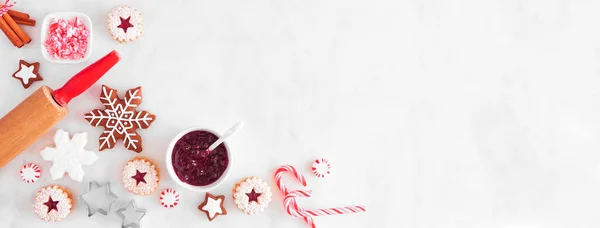 Christmas baking corner border with cookies and sweets. Top view over a white marble background with copy space. Holiday baking concept.