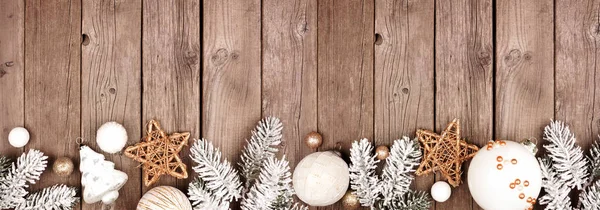 Christmas border of white and gold ornaments with frosty branches. Above view on a rustic wood banner background with copy space.