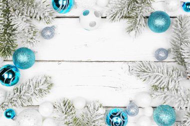 Mavi ve beyaz süslemeleri olan soğuk dallardan oluşan bir Noel çerçevesi. Kopya alanı olan beyaz ahşap bir arkaplanda görünümün üzerinde.