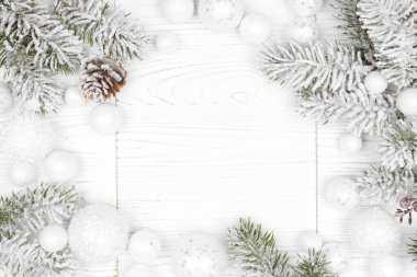 Karlı dalları ve beyaz Noel mücevherleri olan bir kış çerçevesi. Kopya alanı olan beyaz ahşap bir arkaplanda genel görünüm.