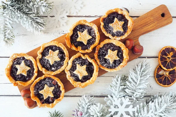 Christmas mincemeat tarts on a serving board. Top view table scene over a white wood background.