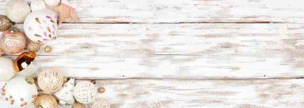 Christmas corner border of gold, white and blush ornaments. Overhead view on a rustic white wood banner background. Copy space.