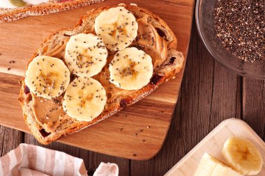 Fıstık ezmeli, muzlu ve chia tohumlu sağlıklı kahvaltı tostu. Koyu ahşap arka planda üst görünüm.