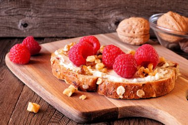 Krem peynirli, fındıklı ve ahududu ekmekli sağlıklı kahvaltı tostu. Koyu renk ahşap arka planda kapat..