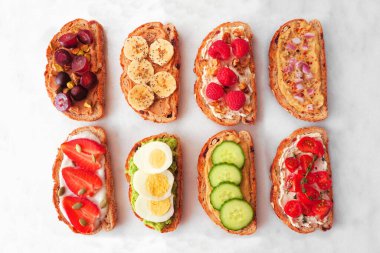 Çeşitli protein yayılımı, meyve, fındık ve sebzeli sağlıklı tost. Beyaz mermer arka planda genel görünüm.