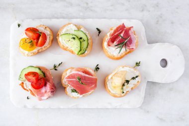 Bir tabak krem peynirli crostini aperatifleri ve çeşitli malzemeler. Beyaz mermer arka planda yukarıdan görüş. Parti yemeği konsepti.