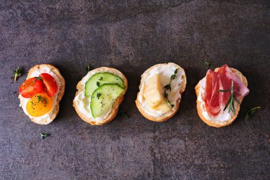 Çeşitli malzemelerle krem peynirli crostini aperatifleri. Koyu taştan bir arka planda üst görünüm. Parti yemeği konsepti.