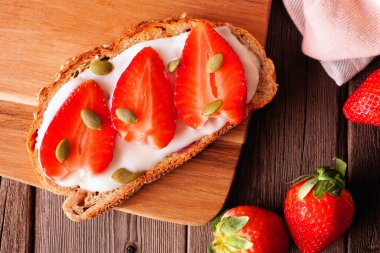 Yoğurtlu sağlıklı çilekli tost ve çoklu tahıllı ekmeğin üzerinde kabak çekirdeği. Koyu bir ahşap arka planda genel görünüm.