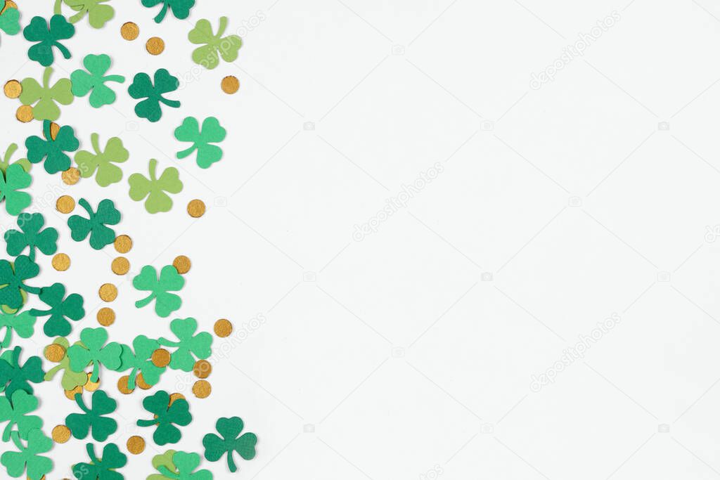 St Patricks Day shamrock and gold coin confetti side border. Overhead view on a white background with copy space.