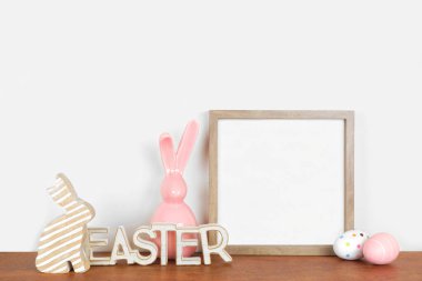 Ahşap bir rafta Paskalya süsleriyle ahşap çerçeve yap. Kırsal ahşap dekorlar, yumurtalar, modern cam tavşanlar. Beyaz bir duvara karşı kare çerçeve. Boşluğu kopyala.