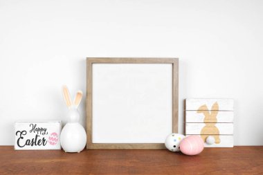 Ahşap bir rafta Paskalya dekoruyla ahşap çerçeve yap. Kalitesiz ahşap tabelalar, yumurtalar, modern cam tavşanlar. Beyaz bir duvara karşı kare çerçeve. Boşluğu kopyala.
