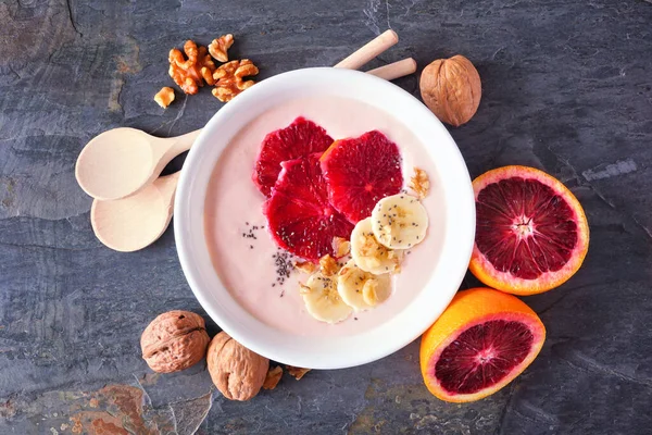 Healthy blood orange and banana smoothie bowl with walnuts and chia seeds. Above view table scene on a dark background.