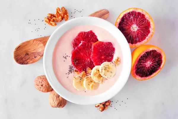 Healthy blood orange and banana smoothie bowl with walnuts and chia seeds. Top view table scene on a bright background.