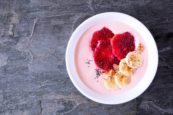 Healthy blood orange and banana smoothie bowl with walnuts and chia seeds. Top view on a dark slate background.