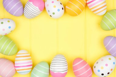 Yumuşak sarı ahşap zemin üzerine renkli Paskalya yumurtası çerçevesi. Kopyalama alanı ile üstten aşağı görünüm.