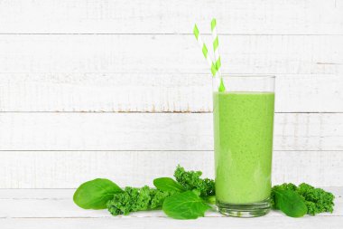 Lahanalı yeşil smoothie ve bardakta ıspanak. Beyaz ahşap arka planda malzemelerle yan görünüm.