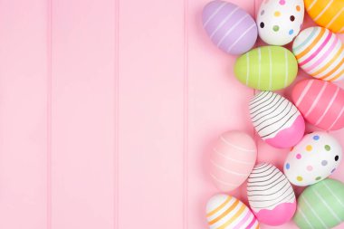 Yumuşak pembe ahşap arka planda renkli Paskalya yumurtası kenarı. Kopyalama alanı ile üstten aşağı görünüm.