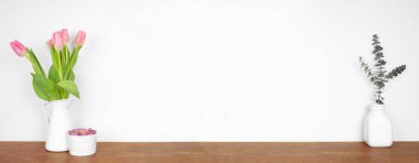 Rafta ev dekorasyonu. Lale çiçekleri, sulu bitkiler ve okaliptüs dalları. Beyaz bir duvara karşı ahşap bir raf. Kopyalama alanı olan pankart.