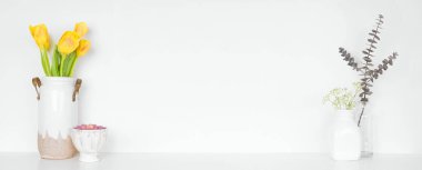 Rafta ev dekorasyonu. Çiçekler, dallar ve bitkiler. Beyaz bir duvara karşı beyaz bir raf. Kopyalama alanı olan pankart.