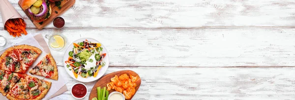 Healthy plant based fast food corner border. Top view over a white wood banner background. Table scene with cauliflower crust pizza, bean burgers, bell pepper nachos, cauliflower wings. Copy space.