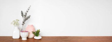 Rafta ev dekorasyonu. Vazolar, sulu bitkiler, çiçekler ve dallar. Beyaz bir duvara karşı ahşap bir raf. Kopyalama alanı olan pankart.