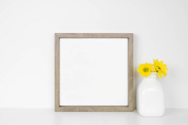 Kare ahşap çerçeveyi sarı papatya çiçekleri vazosuyla süsleyin. Beyaz bir duvara karşı beyaz bir raf. Boşluğu kopyala.