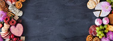 Anneler Günü şarküterisi, arka planda siyah pankarta karşı iki sınır çiziyor. Çeşit çeşit peynir, et, meyve ve tatlı mezeler. Boşluğu kopyala.