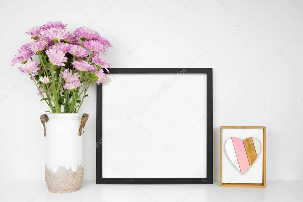 Mock up black frame with vase of purple mum flowers and heart decor. Mother's Day decor theme. White shelf against