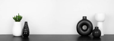 Modern siyah-beyaz ev dekorasyonu ve raftaki bitkiler. Beyaz bir duvara karşı siyah bir raf. Kopyalama alanı olan pankart.