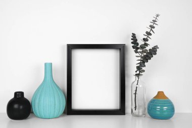 Okaliptüs dalları ve siyah ve mavi dekoru olan siyah bir çerçeve yap. Beyaz bir duvara karşı beyaz bir raf. Boşluğu kopyala.