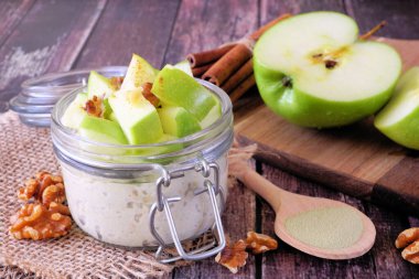 Bir gecelik yulaf, kibrit ve kavanozda yeşil elma. Kırsal ahşap arka planda masa sahnesi.