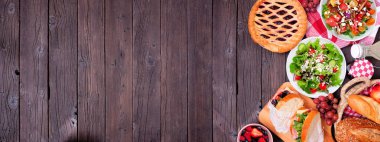 Yaz pikniği yan sınırı. Ahşap bir arka planda genel manzara. Soğuk salata, sandviç, meyve ve ikramlar. Boşluğu kopyala.