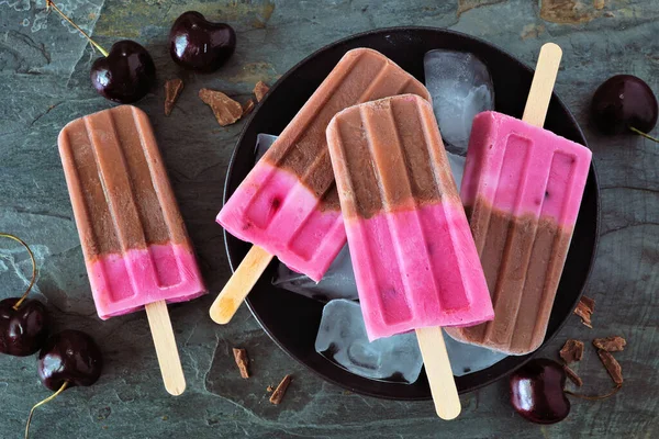 Plate of chocolate and cherry ice pops. Close up above view table scene on a dark stone background.