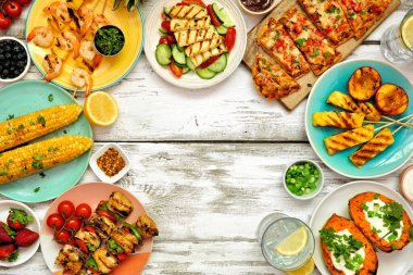 Beyaz ahşap arka planda yaz barbekü ızgarası çerçevesi. Tavuk ve karides şişleri, yassı ekmek, doldurulmuş tatlı patates, ızgara meyve, mısır ve salata. Kopyalama alanı ile üstten aşağı görünüm.