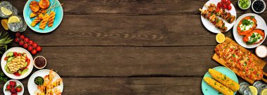 Yazın barbekü ızgarası koyu ahşap kaplama arka planda çifte sınır. Kızarmış ekmek, tavuk ve karides şişi, doldurulmuş tatlı patates, mısır, meyve ve salata. Kopyalama alanı ile üstten aşağı görünüm.