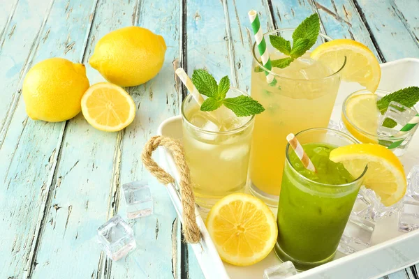 Tray of cool summer iced green tea and lemonade drinks against a rustic blue wood background