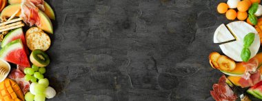 Yaz meyveleri temalı şarküteri köşe sınırı koyu bir arka plana karşı. Meyve, peynir ve meze karışımı. Boşluğu kopyala.