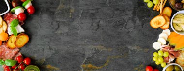 İtalyan temalı şarküteri, arka planda koyu bir pankarta karşı çifte sınır. Karışık peynir, et ve meyve mezeleri. Kopyalama alanı ile görünümün üstünde.