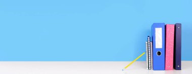 Okul klasörleri, not defterleri ve kalem beyaz bir rafta mavi pankartın önünde. Okul konseptine geri dönelim. Boşluğu kopyala.