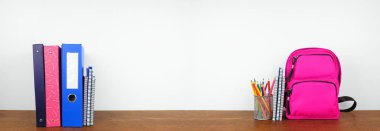 Okul gereçleri ve sırt çantası tahta bir rafta beyaz pankartın önünde. Okul konseptine geri dönelim. Boşluğu kopyala.