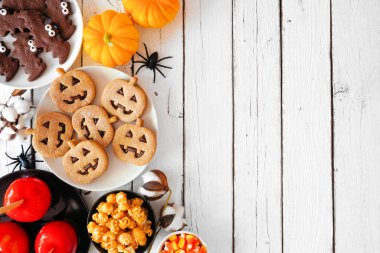 Geleneksel Cadılar Bayramı, beyaz ahşap zemin üzerinde fotokopi alanı olan kenar sınırlara bakar. Manzaranın üstünde. Elma şekeri, kurabiye, şeker ve şeker çeşitleri.